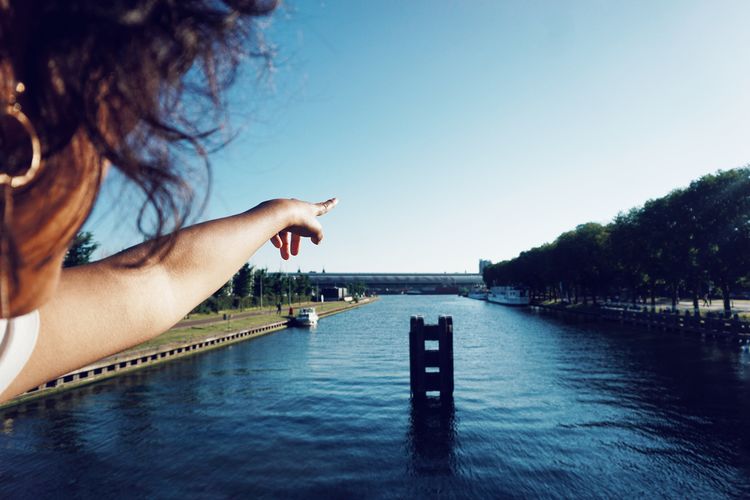 Midsection of woman gesturing over lake against clear sky