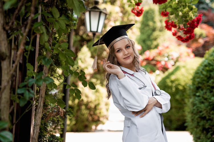 Portrait of woman wearing graduation gown standing against trees