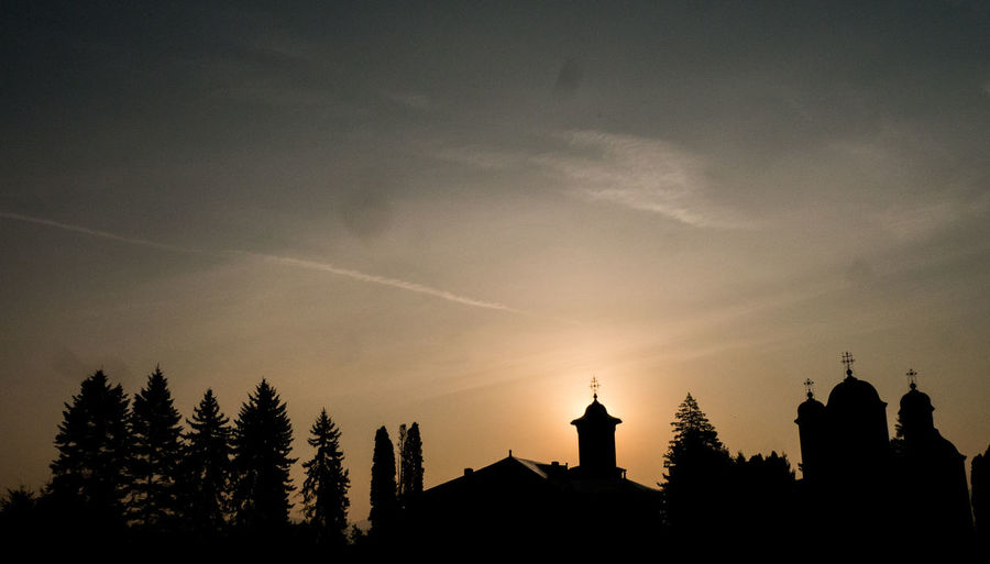 Low angle view of silhouette buildings and church against sky during sunset