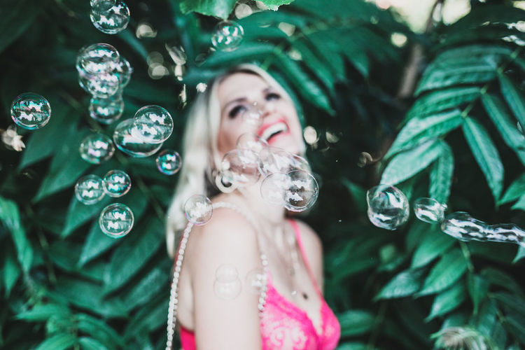 Close-up of bubbles by smiling woman standing against plants