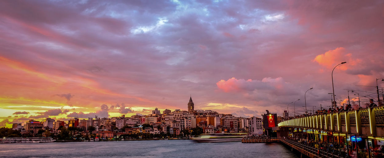 Galata bridge over river leading towards cityscape against cloudy sky during sunset