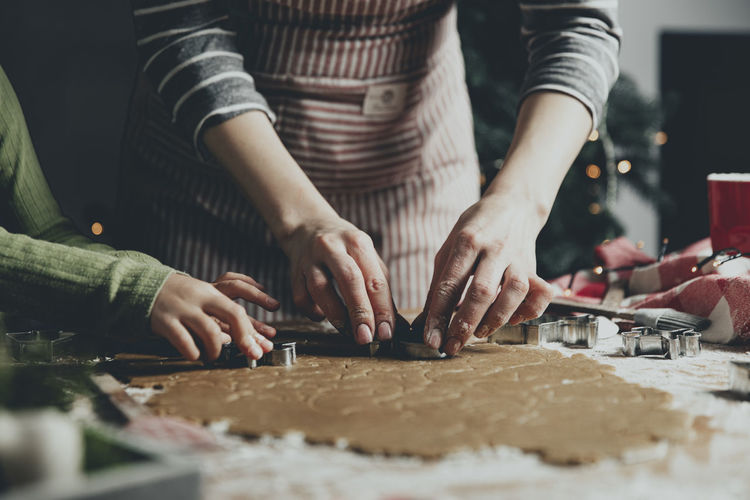Mother and daughter or sisters cooking gingerbread cookies on wooden table at kitchen