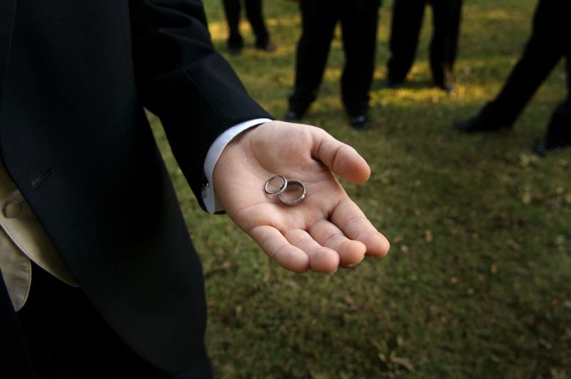 Midsection of bridegroom holding wedding rings on field