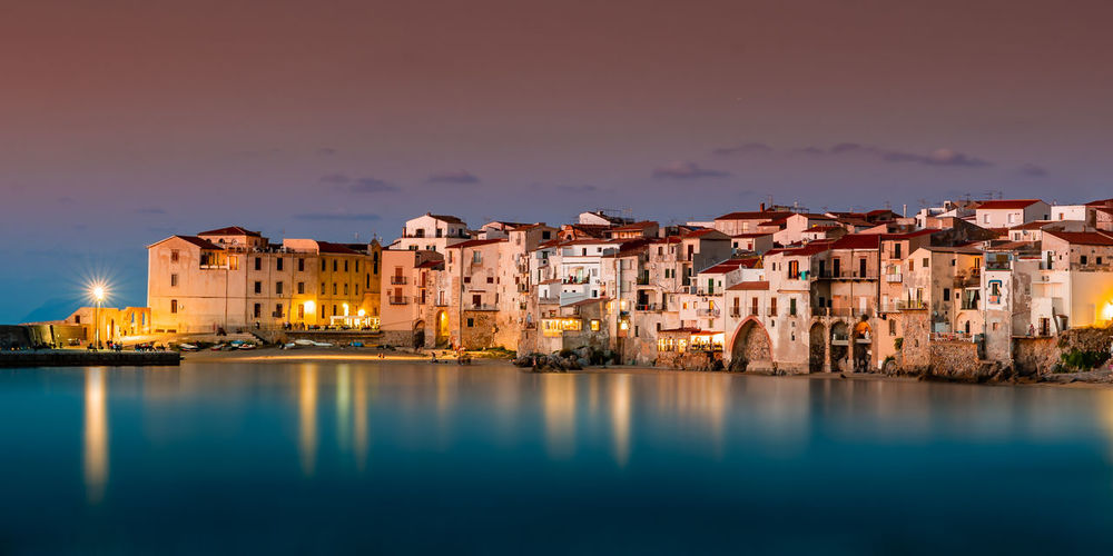 Buildings by lake in city at dusk