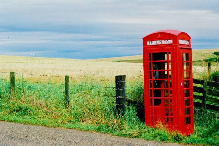 Red telephone booth on field against sky