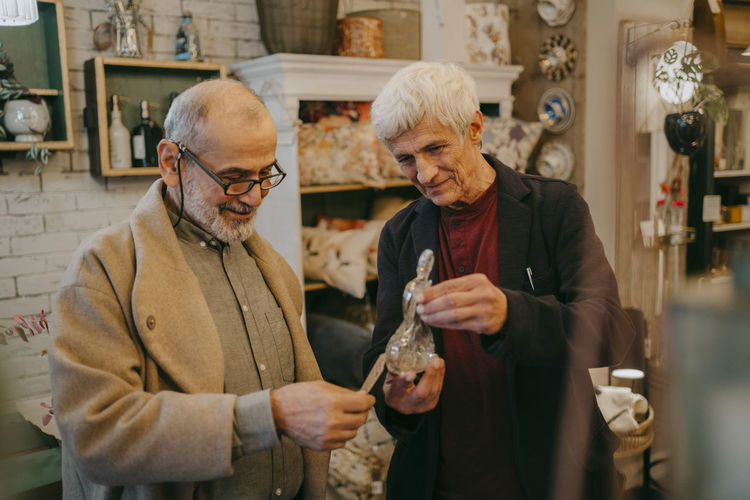 Senior male customer checking price tag of glass figurine held by owner at store