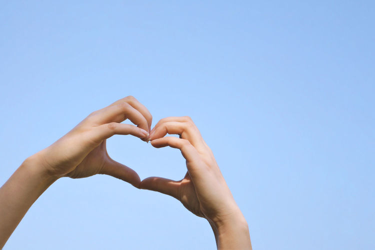 Low angle view of hand holding heart shape against clear blue sky