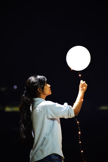 Woman holding illuminated balloon against sky