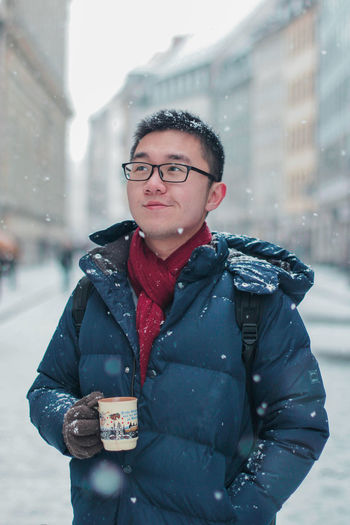 Young man holding mug standing on snow covered road in city
