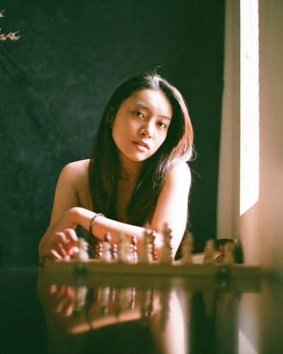 Portrait of young woman sitting by chess pieces on table
