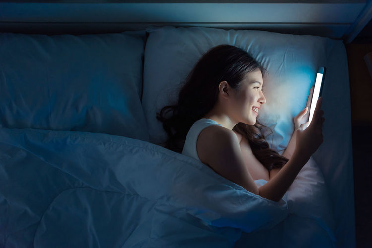 Midsection of woman using mobile phone in bed