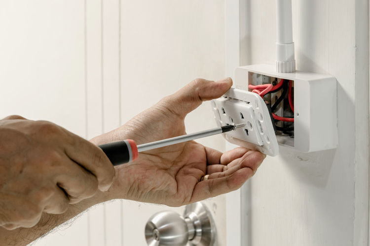 Cropped hands of male electrician repairing electrical outlet on wall