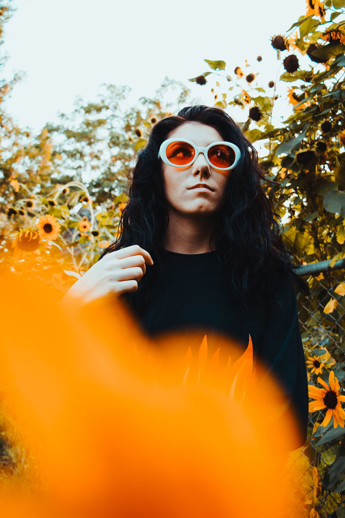 CLOSE-UP PORTRAIT OF YOUNG WOMAN WEARING SUNGLASSES AGAINST TREES