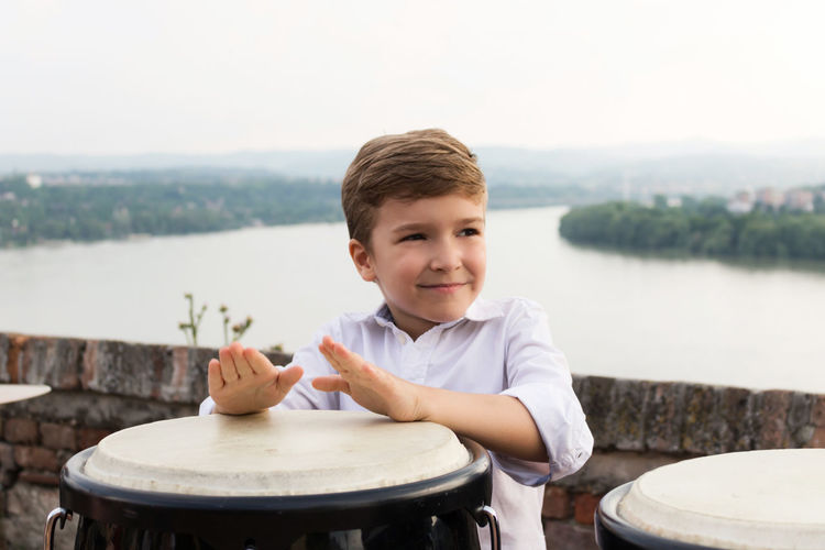 Boy playing bongo against river