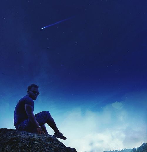 Low angle view of man sitting on rock against sky at night