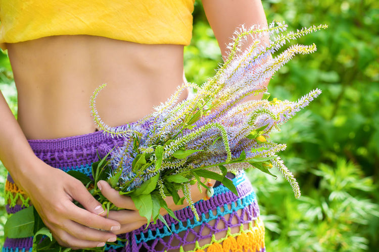 A girl in a knitted skirt and a yellow top holds a bouquet of wild flowers in her hands. 
