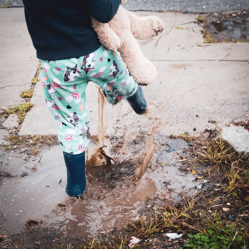 Low section of small child standing in mud puddle splashing water