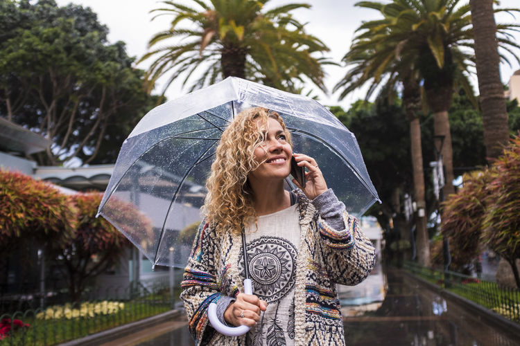 Woman with umbrella talking over phone while standing during rainy season