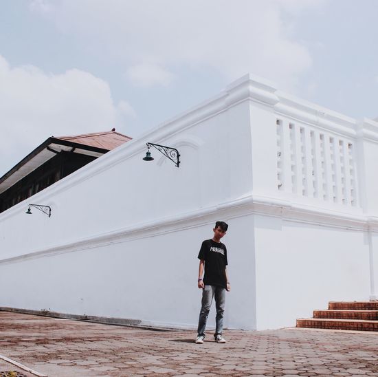 Full length of young man standing by building against sky