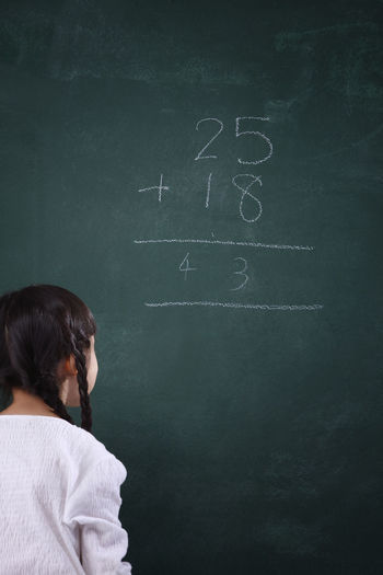 Rear view of girl learning mathematics on blackboard