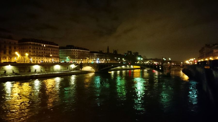Illuminated city by river against sky at night