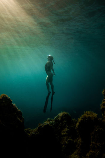 Side view of slim female in swimsuit and flippers swimming underwater in turquoise sea