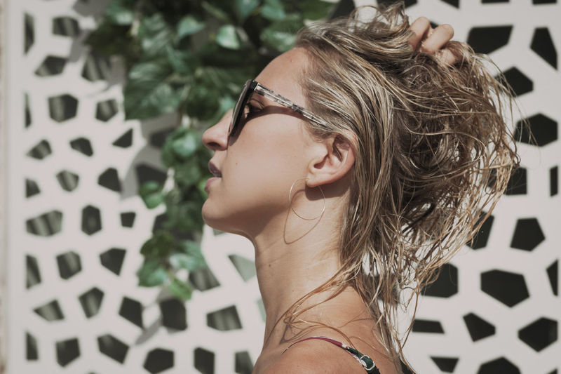 Side view of young woman with hand in hair wearing sunglasses on poolside during sunny day