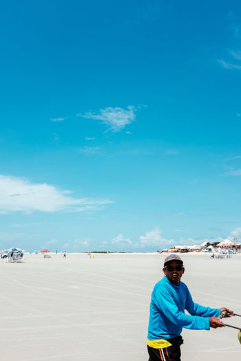 Portrait of man standing on beach against blue sky