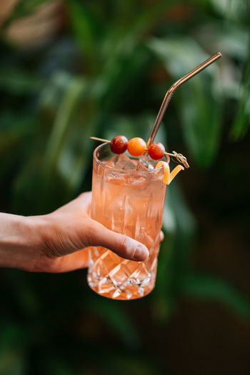 Crop anonymous person demonstrating transparent glass with cold cocktail with ice cubes served with berries on stick and zero waste straw person