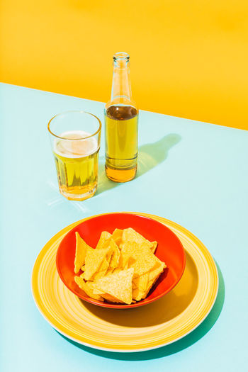 Bowl with crunchy tortilla chips placed near glass and bottle of cold beer