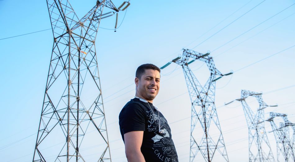 Portrait of man standing by electricity pylon against clear sky