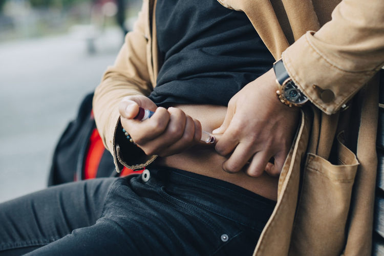 Midsection of man injecting insulin while sitting on bench