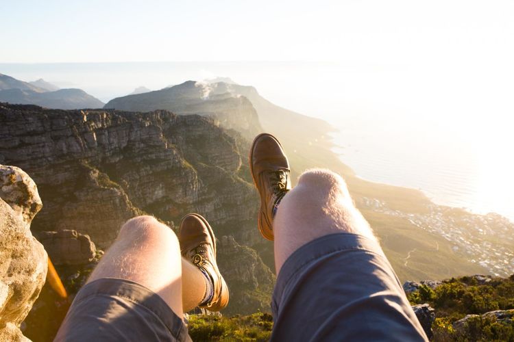 Low section of man sitting at edge of mountain