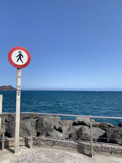 Road sign by sea against clear blue sky