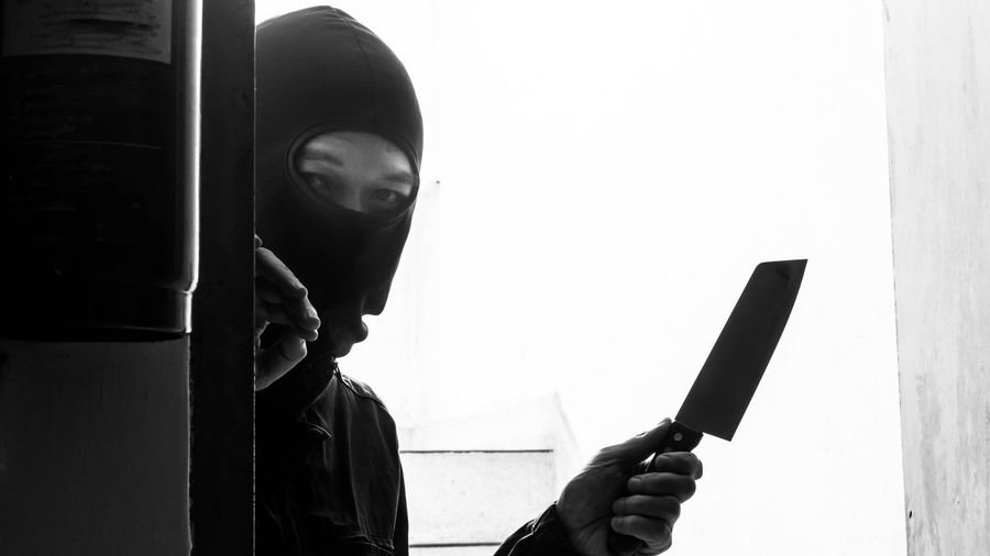 Portrait of robber holding knife while peeking through window