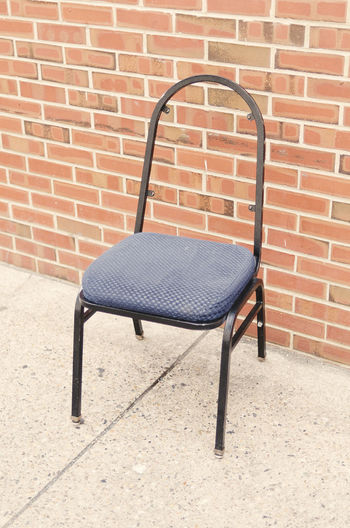 Empty chair against brick wall