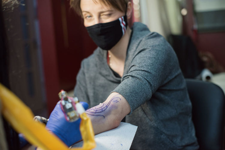 Woman wearing mask getting tattooed at studio