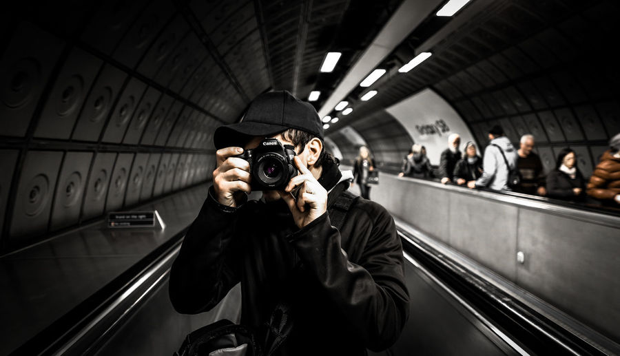 Man photographing while standing on escalator at subway station