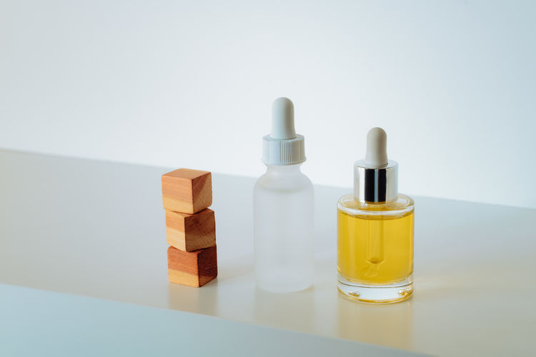 Face serum in matte glass bottle and face oil and stacked wood cedar cubes on white background