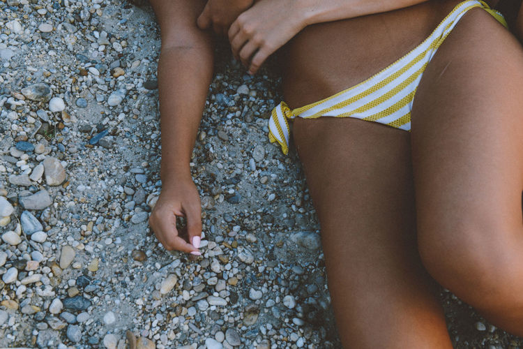 Midsection of women wearing bikini- lying at beach