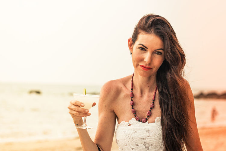 Portrait of mature woman holding drink at beach