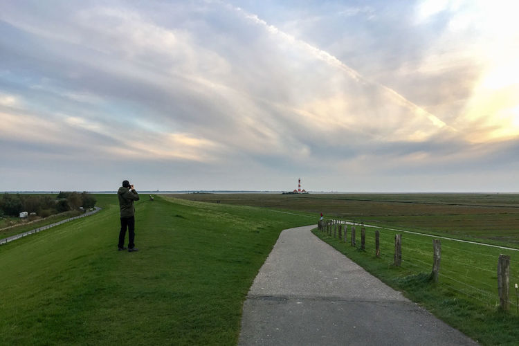 Rear view of man photographing on grassy landscape against sky