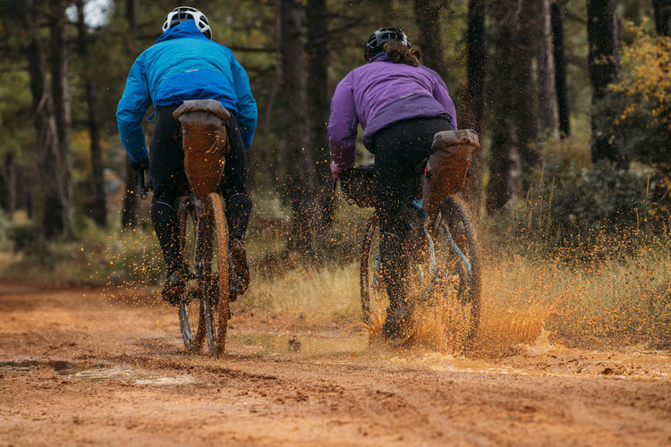 People in protective helmet and colorful jacket riding bikes in forest during bike packing adventure