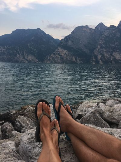 Low section of couple relaxing on rock at lakeshore against mountains