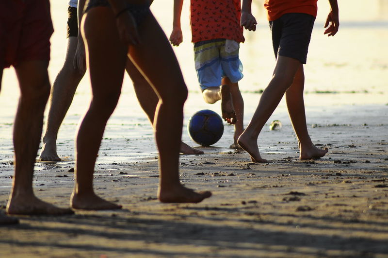 Low section of people playing soccer ball on beach