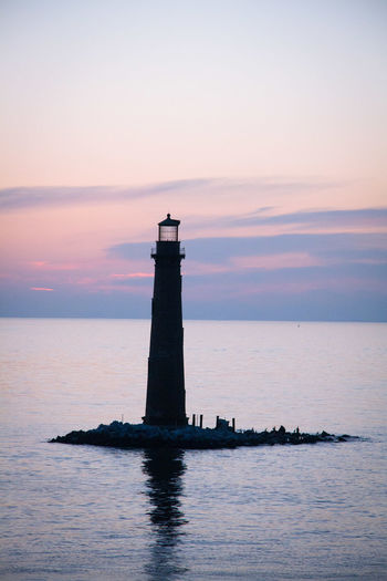 Silhouette lighthouse amidst sea against sky at sunset