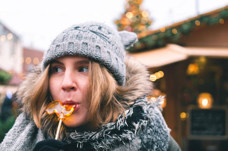 Close-up of thoughtful woman eating lollipop in city during winter