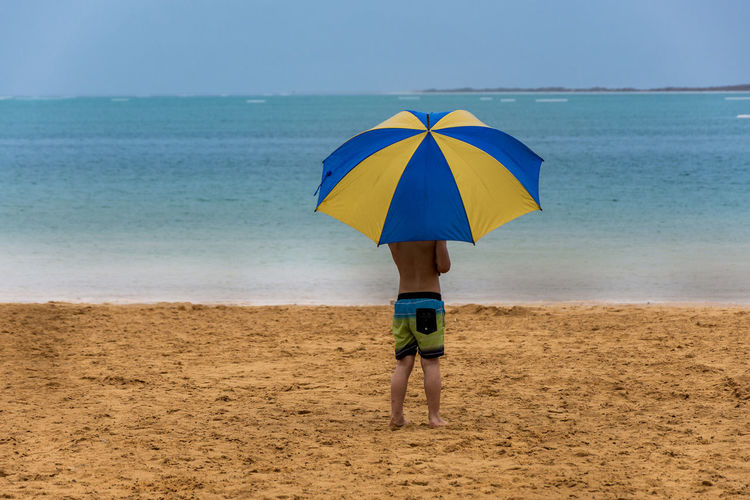 Rear view of boy standing on beach with umbrella