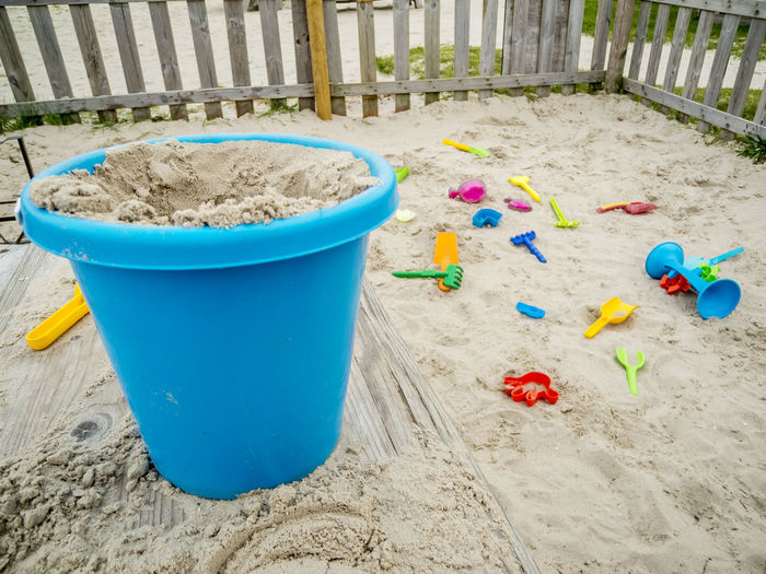 Fenced sandpit on the german north sea coast with blue sand bucket in the foreground.