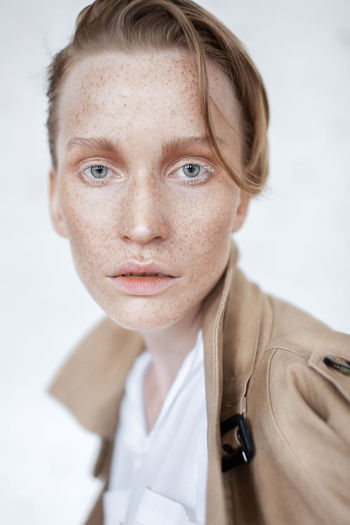Close-up portrait of woman with freckles on face against white background